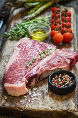 Raw T-bone Steak with fresh herbs and oil on dark wooden background