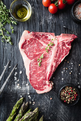 Raw T-bone Steak with fresh herbs and oil on black background, top view