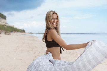 Romantic attractive tanned blond girlfriend walking happily sandy beach enjoy summer vacation tropical island travel, female tourist laughing happily turn camera hold blanket dancing seaside