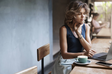 Busy attractive young modern businesswoman prepare project reading article sit near window cafe table drink coffee thinking look laptop display. Female student tutor make arrangements future lesson