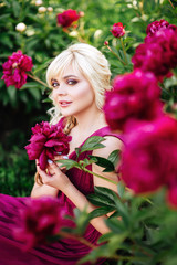 Outdoor close up portrait of beautiful young woman with long blonde hair, makeup, posing in the blooming garden. Female spring fashion concept