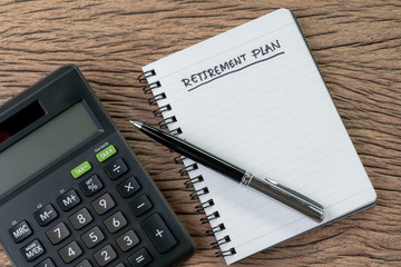 Retirement plan concept, calculator with empty notepad with pen and handwriting headline as Retirement Plan on wood table, plan of saving and investment for expense after retire life