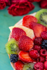 Beautiful delicious sweet cake with berries. Strawberries, kiwi, currants, blackberries, raspberry, pineapple on the biscuit. Fruit variety. Dessert. Bouquet of roses. Soft focus. Macro. Top view.