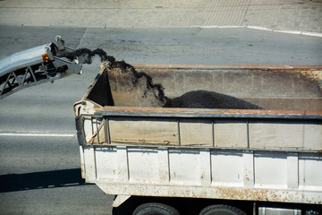 Removing old pavement from a street surface. Road milling machine is loading the truck by asphalt powder. © mihailgrey