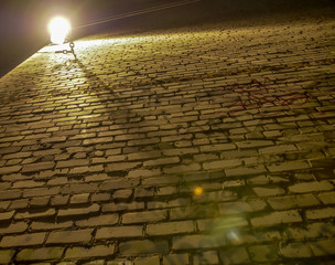 Old rough and uneven brick wall illuminated by a lantern, bottom view