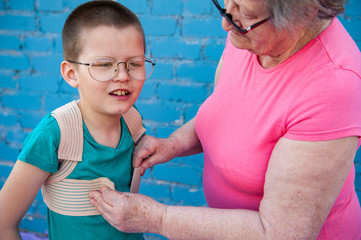 elderly woman in pink T-shirt and glasses wears corset to correct posture for her grandson. child is happy that grandmother loves him and cares