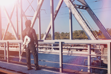 A man with an electric guitar on the railway. A musician in a leather jacket with a guitar on the street in the industrial zone.