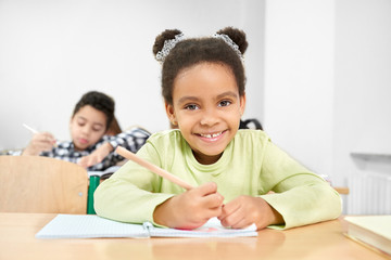 Schoolgirl smiling, posing in classroom at primary school.