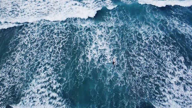 aerial top down view of surfer with surf board catching ocean wave from drone 
