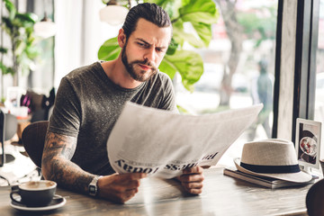 Handsome bearded hipster man reading newspaper with coffee at table in cafe