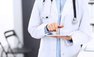 Female physician using digital tablet  while standing near reception desk at clinic or emergency hospital. Unknown doctor woman at work. Medicine concept