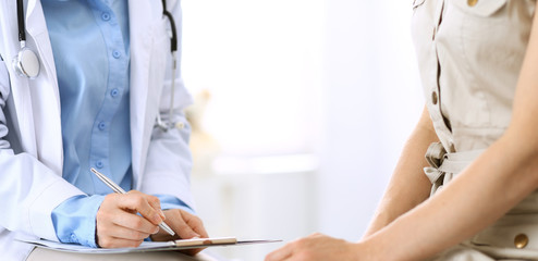 Doctor and patient talking. Physician at work in hospital while writing up medication history records form on clipboard near sitting woman. Healthcare and medicine concepts