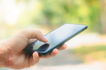 close up handsome man use left hand typing mobile phones and touch screen working with app devices in park with sunrise and green blur nature background.