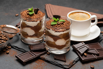 Classic tiramisu dessert in a glass and cup of coffee on dark concrete background