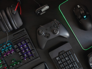 gamer workspace concept, top view a gaming gear, mouse, keyboard, joystick, headset, mobile joystick and mouse pad on black table background with RGB color.