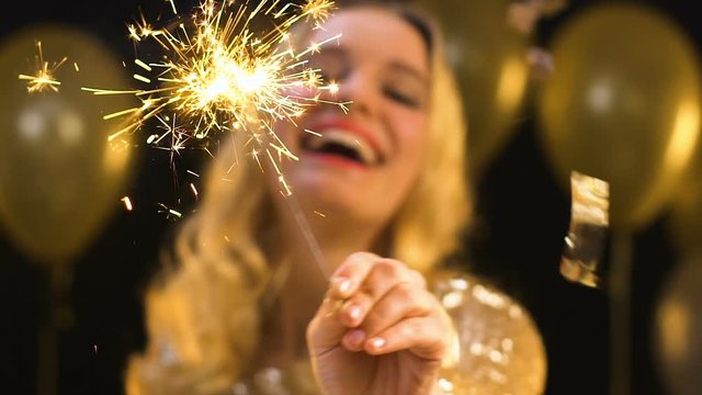 Pretty blond female waving bengal light under falling confetti on party, prom