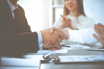 Business people shaking hands at meeting while theirs colleagues clapping and applauding. Group of...