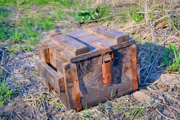 An antique wooden box with rusty metal hardware fittings rests on a grass background.