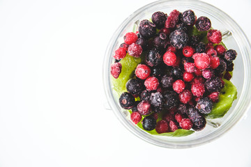 Flat lay of a blender and fresh seasonal berries and fruits over white background, preparing smoothies, detox, healthy clean eating. Summer drinks.