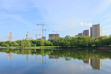 Naklejka premium Construction of residential buildings with cranes against the blue sky in the early morning and reflected in the pond