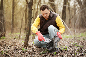 Charity volunteer picks up litter in forest, caring for nature. Spring cleaning in park, outdoor trash and rubbish.