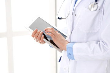 Woman doctor using tablet computer while standing straight in hospital closeup. Healthcare, insurance and medicine concept
