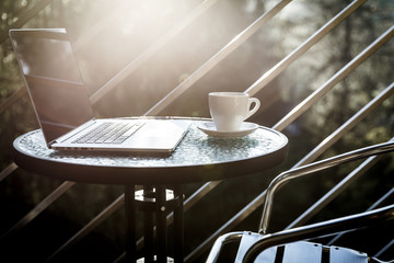 White tea or coffee mug and a laptop on a balcony coffee table