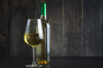 Transparent bottle of white dry wine on the table. White wine glass on a wooden background.