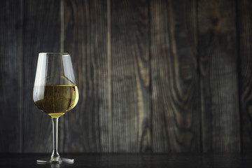 Transparent bottle of white dry wine on the table. White wine glass on a wooden background.