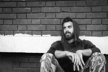 Homeless man drug and alcohol addict sitting alone and depressed on the street leaning against...