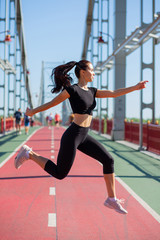 Fototapeta na wymiar Sporty brunette girl jumping on the jogging track