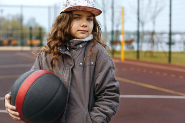 Little girl holding basketball ball at the street playground. Space for text