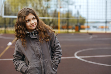 Merry little girl with curly hair standing on a street playground. Space for text