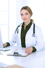 Young woman doctor at work in hospital looking at desktop pc monitor. Physician controls medication history records and exam results. Medicine and healthcare concept