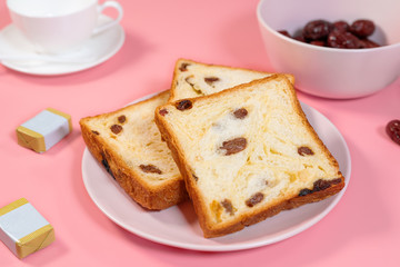 Raisin toast, butter and tea cup placed on pink table