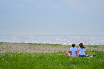 海岸で芝生の上に座る若いカップル、爽やかな夏の海。