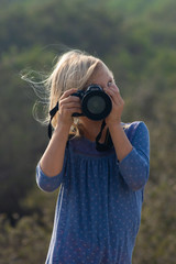 Young girl in nature taking pictures with a large dslr and a zoon lens.