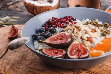 Rice coconut porridge with figs, berries, nuts, dried apricots and coconut milk in plate on rustic wooden background. Healthy breakfast ingredients. Clean eating, vegan food concept, close up
