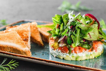 Healthy fresh salad with avocado, salmon, greens, arugula, spinach and cheese with  toast in plate over dark background. Healthy vegan food, clean eating, dieting