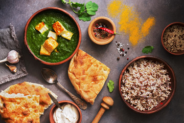 Palak paneer or Spinach and Cottage cheese curry, rice, spices , naan, on a dark background. Traditional Indian food. Overhead view, copy space.
