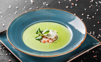 Broccoli green cream soup with shrimp and cheese in plate on dark stone background. Clean eating, healthy food concept. Top view