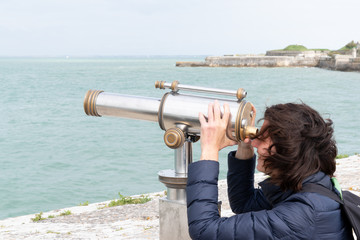 tourist woman looking through a coin operated binoculars on the sea vacation