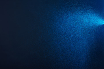 Dark blue background with abstract sparkling powder, dispersed in air. Water spray, lit by light.
