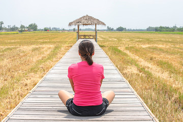 Woman sitting on a wooden bridge with a bamboo hut in the rice fields.