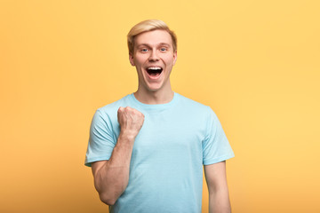 positive gorgeous young emotional man raising clenched fists in hooray gesture, rejoicing at his success. lick, happiness concepts , winner celebrating his victory