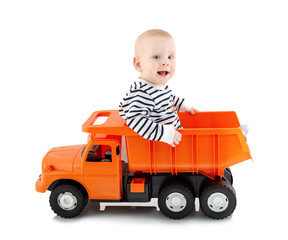 Happy young boy sitting in open-box bed of tipper truck toy, isolated on white background with shadow reflection. Toddler sits on a dumper truck. Adorable small boy drives a truck.