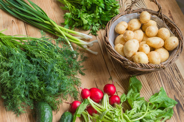 Fresh raw organic vegetables: potatoes, radishes, green onions, cucumbers on a wooden background.