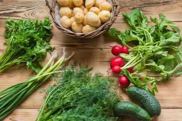 Fresh raw organic vegetables: potatoes, radishes, green onions, cucumbers on a wooden background.