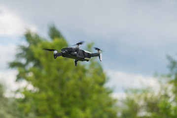 Flying drone in against the sky and green trees.