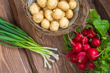 Fresh raw organic vegetables: potatoes, radishes, green onions on a wooden background.